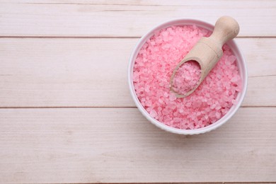 Photo of Bowl and scoop with pink sea salt on white wooden table, top view. Space for text