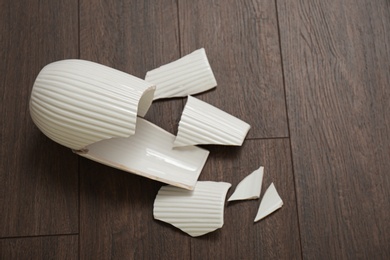 Broken white ceramic vase on wooden floor, above view