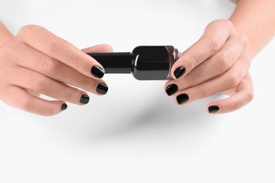 Photo of Woman with black manicure holding nail polish bottle on white background, closeup