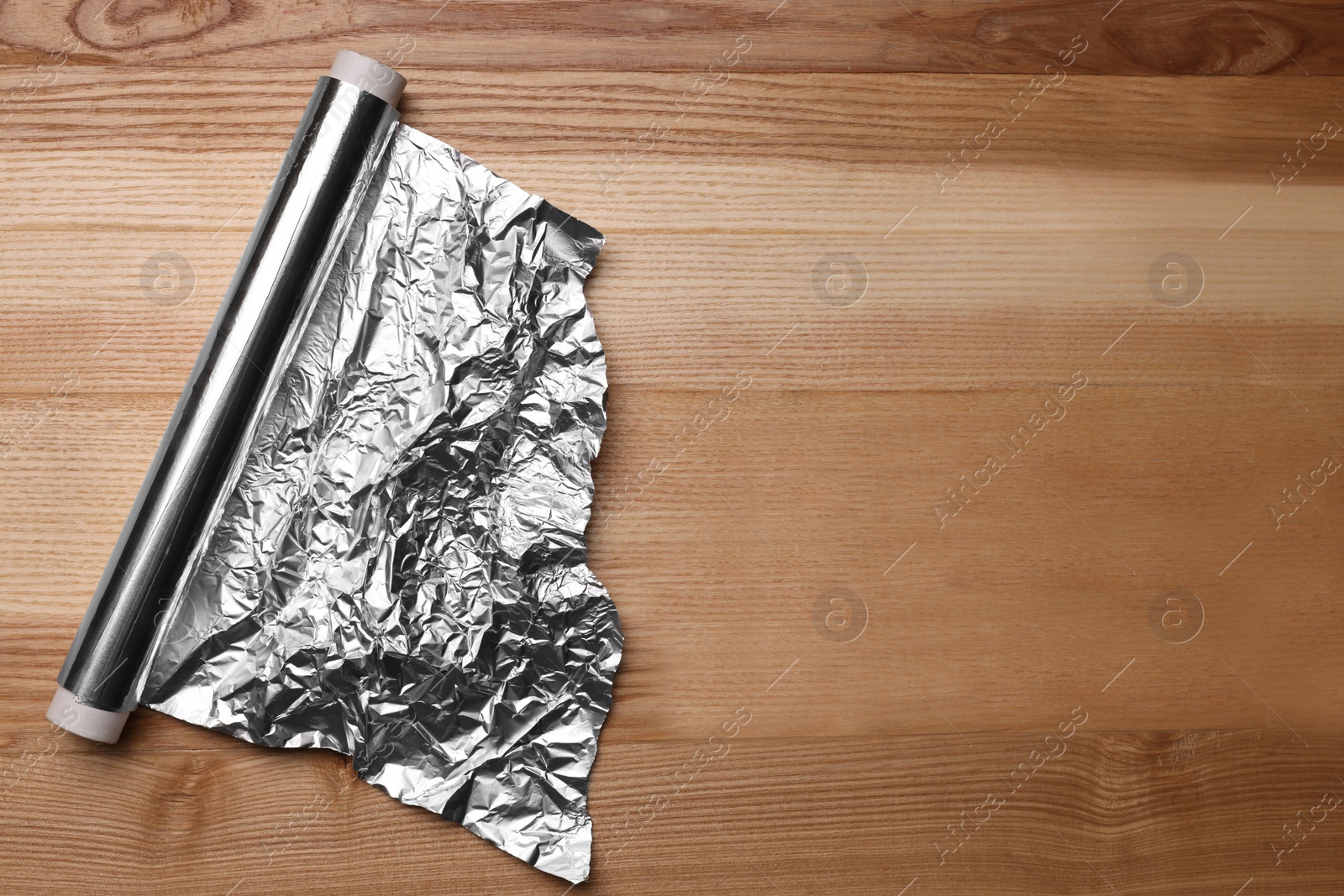 Photo of Roll of aluminum foil on wooden table, top view. Space for text