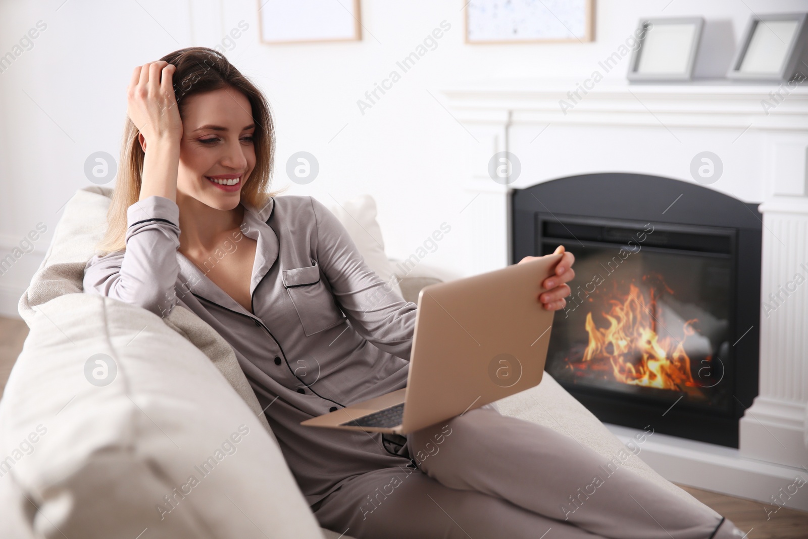 Photo of Young woman with laptop on sofa near fireplace at home