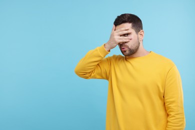 Photo of Embarrassed man covering face on light blue background. Space for text