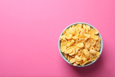 Photo of Bowl of tasty crispy corn flakes on pink background, top view. Space for text