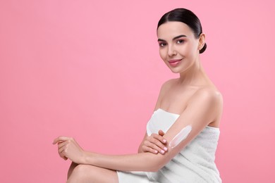 Photo of Beautiful woman with smear of body cream on her arm against pink background, space for text