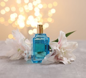 Photo of Bottle of perfume and beautiful lily flowers on table against beige background with blurred lights