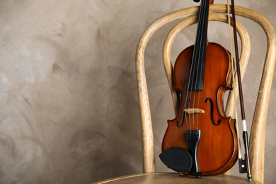 Photo of Classic violin and bow on chair against beige background. Space for text