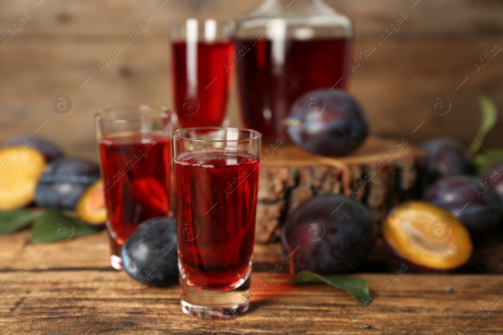 Photo of Delicious plum liquor and ripe fruits on wooden table. Homemade strong alcoholic beverage