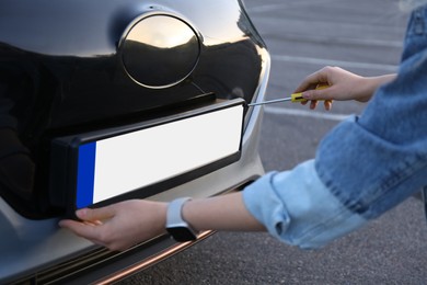 Woman with screwdriver installing vehicle registration plate to car outdoors, closeup
