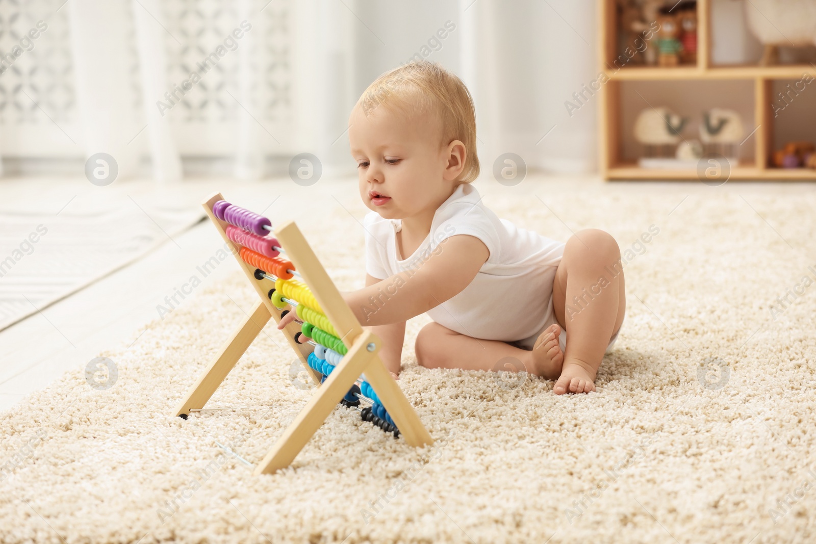 Photo of Children toys. Cute little boy playing with wooden abacus on rug at home