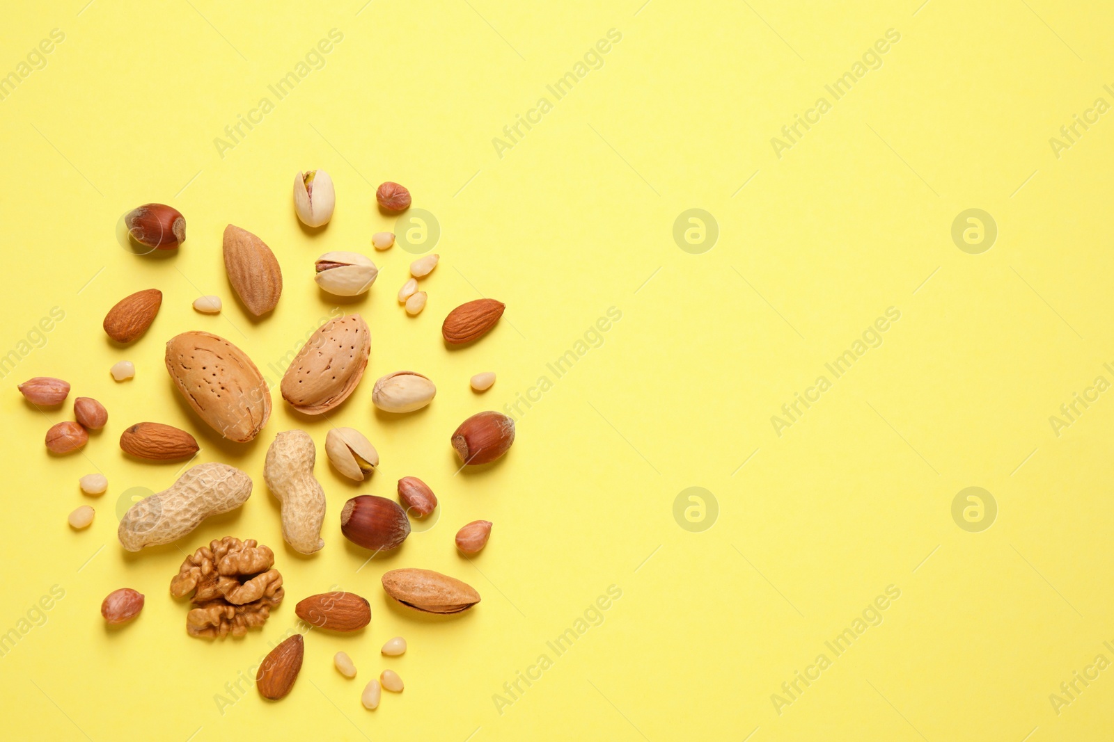 Photo of Different delicious nuts on yellow background, flat lay. Space for text