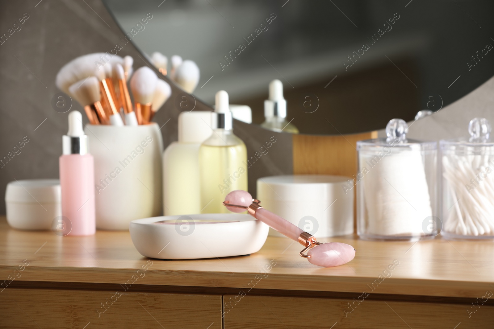 Photo of Natural face roller and cosmetic products on wooden dressing table