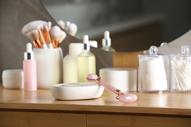 Photo of Natural face roller and cosmetic products on wooden dressing table