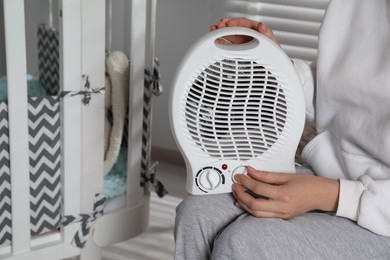 Photo of Young woman adjusting temperature on modern electric fan heater in child room, closeup. Space for text
