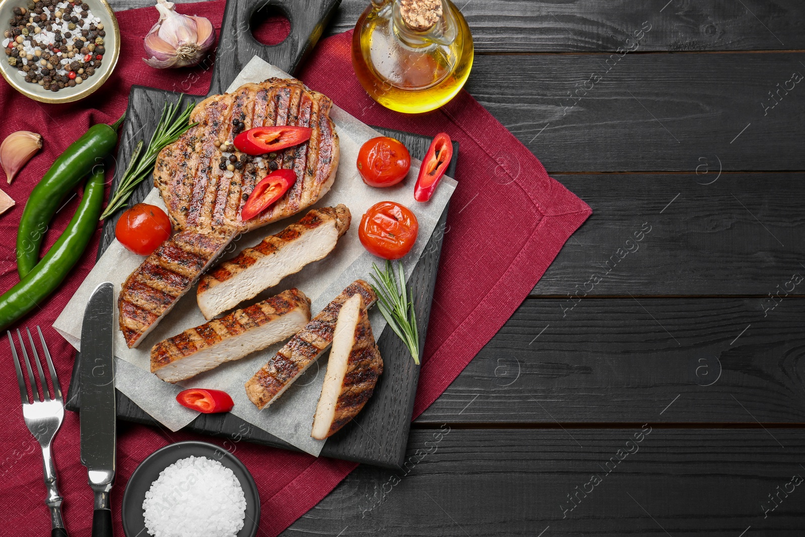 Photo of Grilled pork steaks with rosemary, spices, vegetables and cutlery on dark wooden table, top view. Space for text