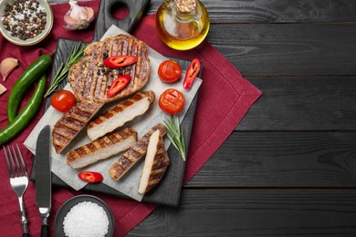 Photo of Grilled pork steaks with rosemary, spices, vegetables and cutlery on dark wooden table, top view. Space for text