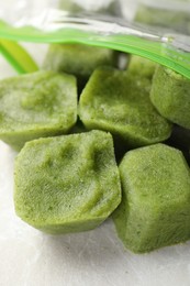 Photo of Frozen broccoli puree cubes in plastic bag on table, closeup