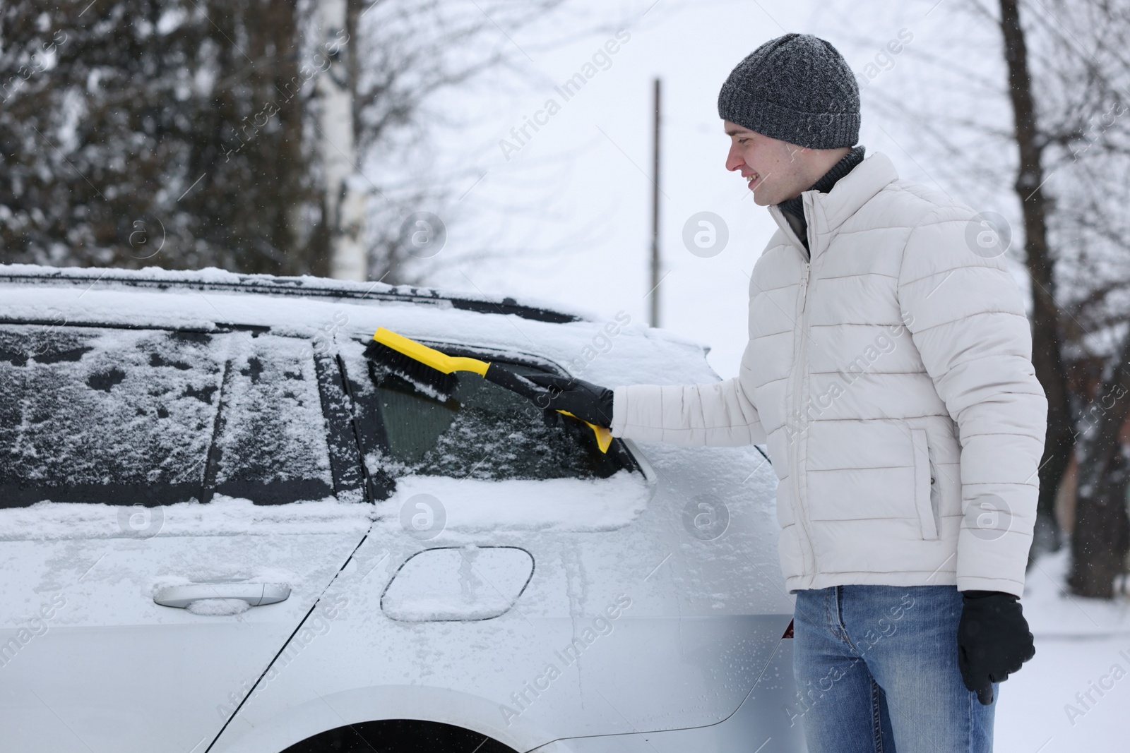 Photo of Man cleaning snow from car with brush outdoors