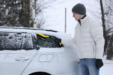 Photo of Man cleaning snow from car with brush outdoors