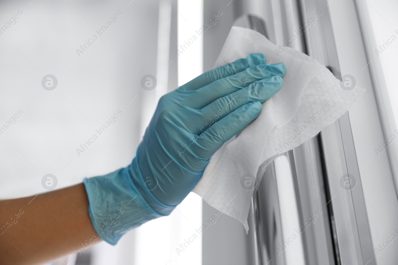 Photo of Woman cleaning door handle with wet wipe indoors, closeup