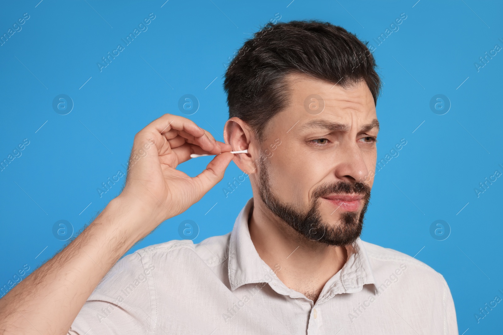 Photo of Emotional man cleaning ears on light blue background