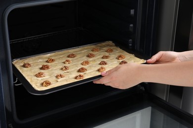 Woman putting baking pan with baklava into oven, closeup