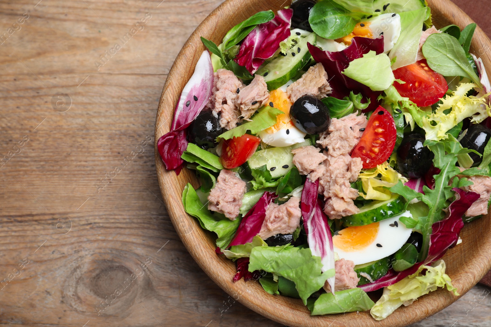 Photo of Bowl of delicious salad with canned tuna and vegetables on wooden table, top view. Space for text