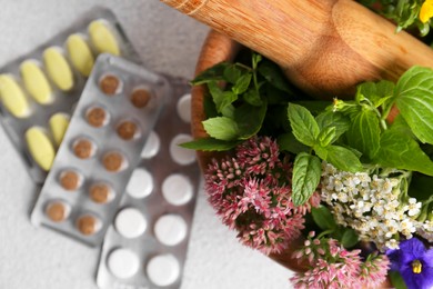 Photo of Wooden mortar with fresh herbs, flowers and pills on white table, top view