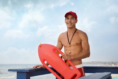 Photo of Handsome lifeguard with life buoy on watch tower against sky