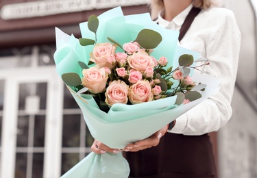 Female florist holding bouquet of beautiful flowers near shop