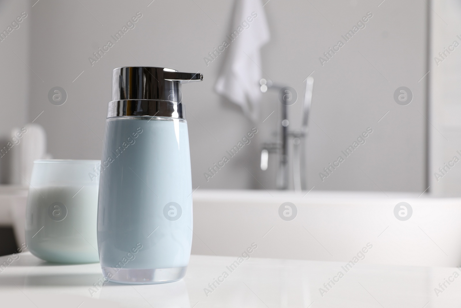 Photo of Dispenser of liquid soap on white table in bathroom, space for text