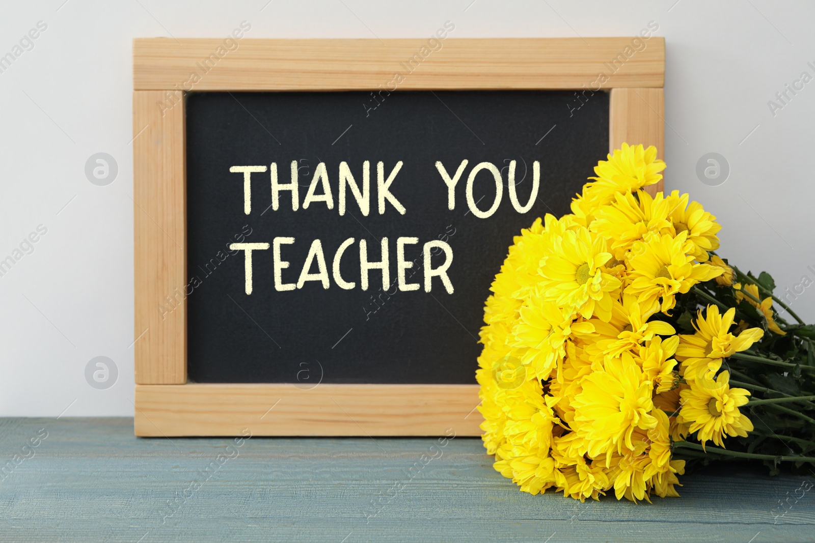 Image of Blackboard with phrase Thank You Teacher and flowers on table near white wall