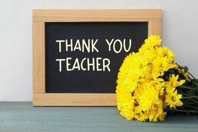 Image of Blackboard with phrase Thank You Teacher and flowers on table near white wall