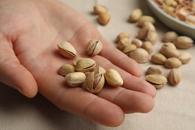 Photo of Woman holding tasty roasted pistachio nuts at table, closeup