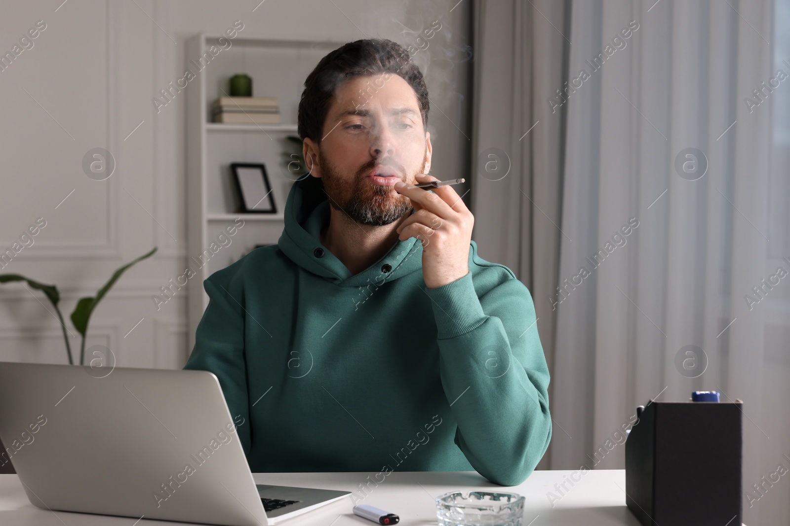 Photo of Man using cigarette holder for smoking at workplace in office