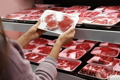 Photo of Woman taking packed pork meat from shelf in supermarket