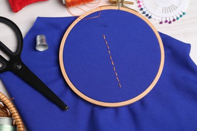 Blue cloth with stitches, sewing thread, needle and scissors on light table, flat lay