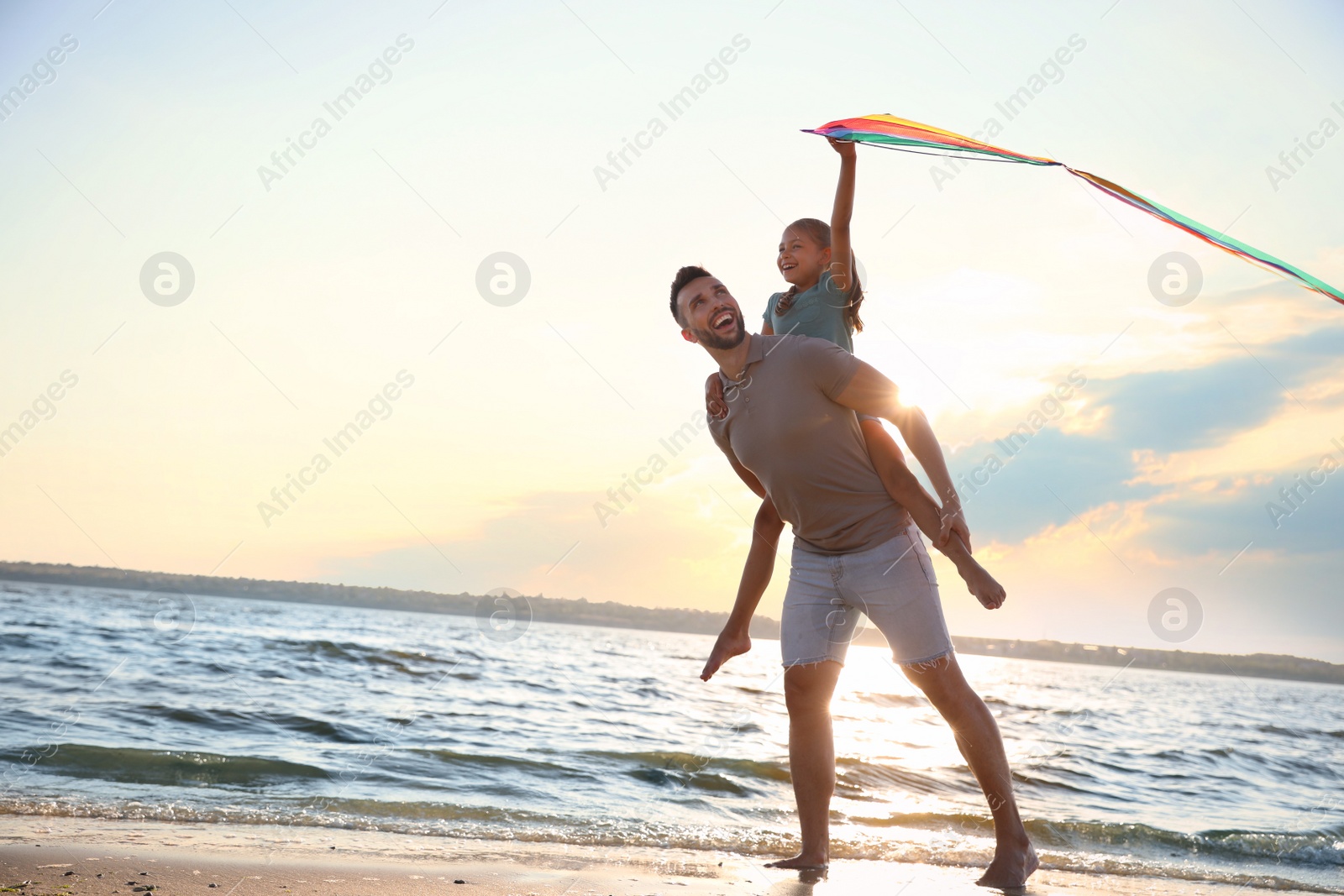 Photo of Happy father and his child playing with kite on beach near sea. Spending time in nature