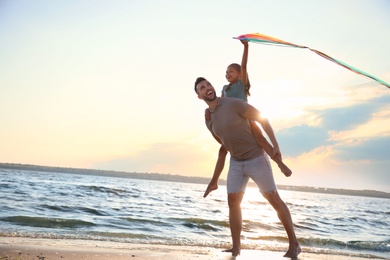 Photo of Happy father and his child playing with kite on beach near sea. Spending time in nature