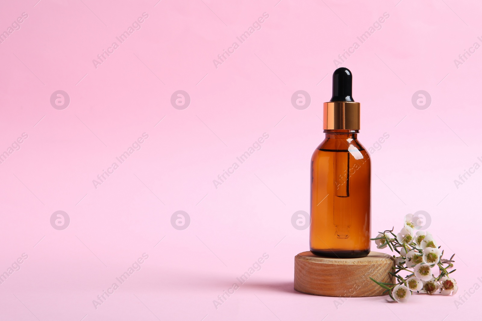 Photo of Bottle with cosmetic oil and flowers on pink background. Space for text