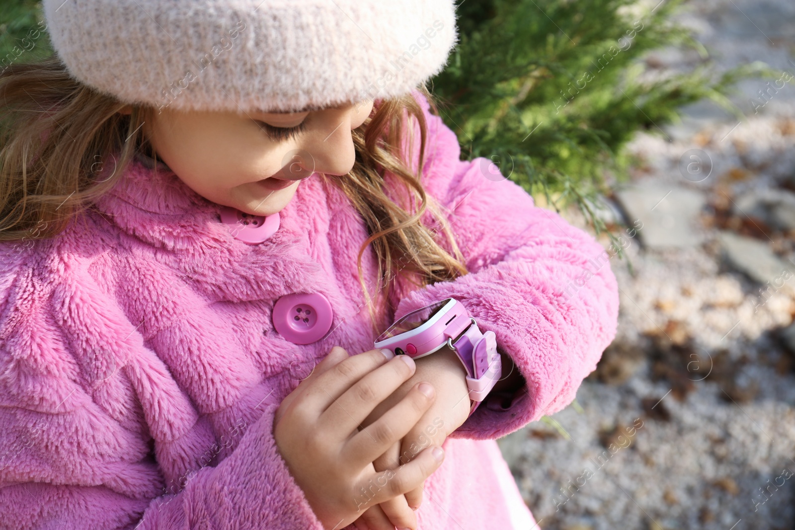 Photo of Little girl using smart watch outdoors, closeup