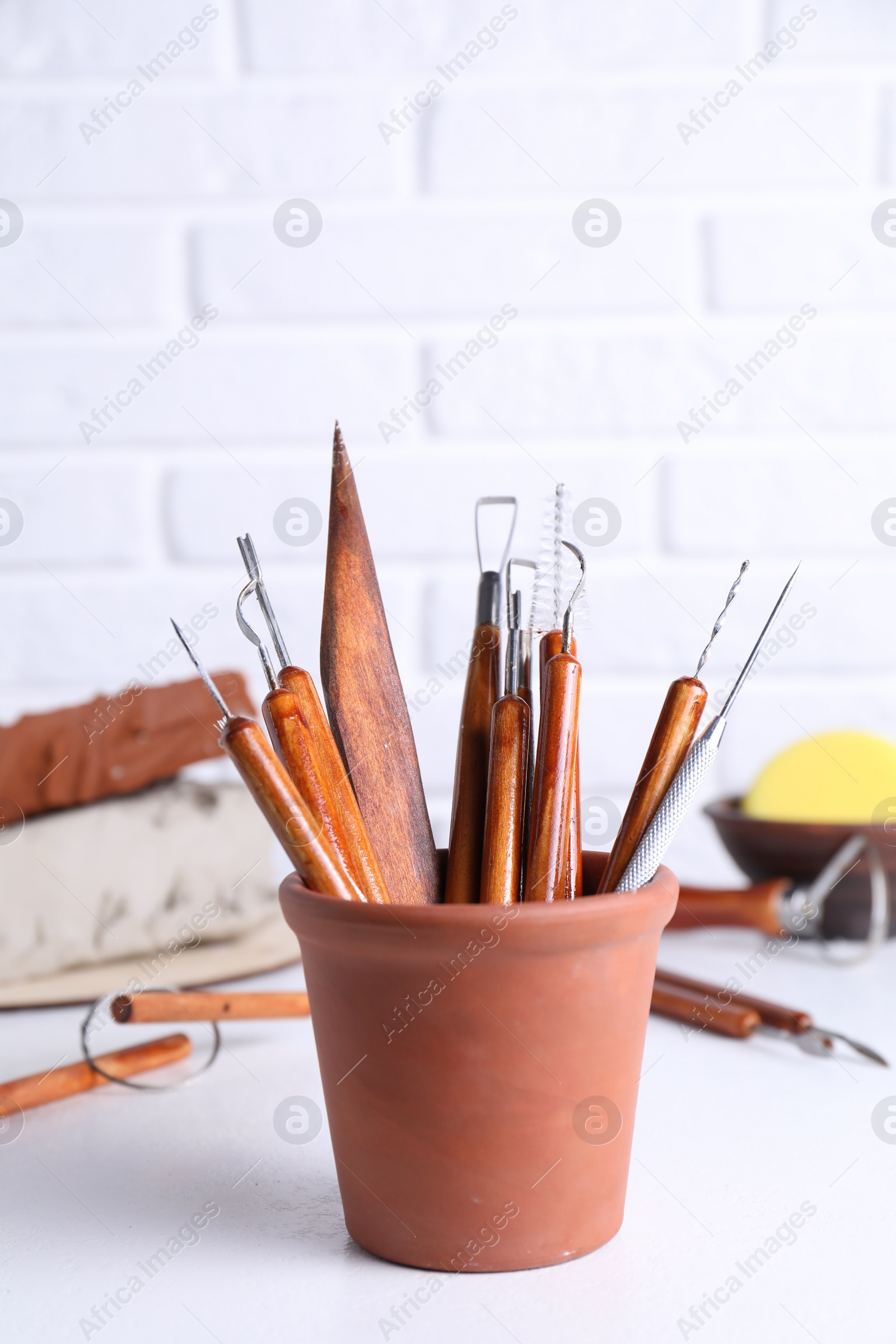 Photo of Clay and set of crafting tools on white textured table against brick wall, closeup