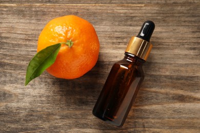 Photo of Bottle of tangerine essential oil and fresh fruit on wooden table, flat lay