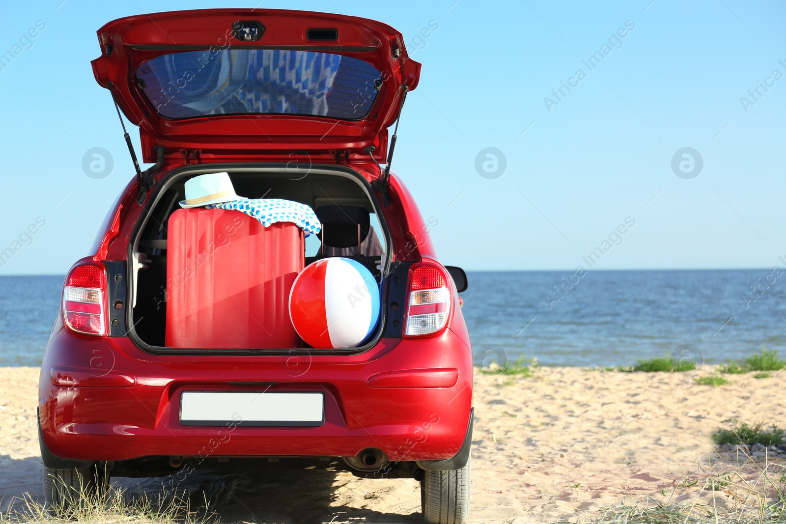 Photo of Suitcase and beach accessories in car trunk on sand near sea. Space for text