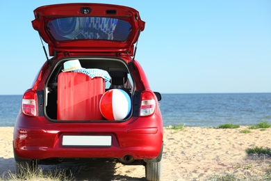 Photo of Suitcase and beach accessories in car trunk on sand near sea. Space for text