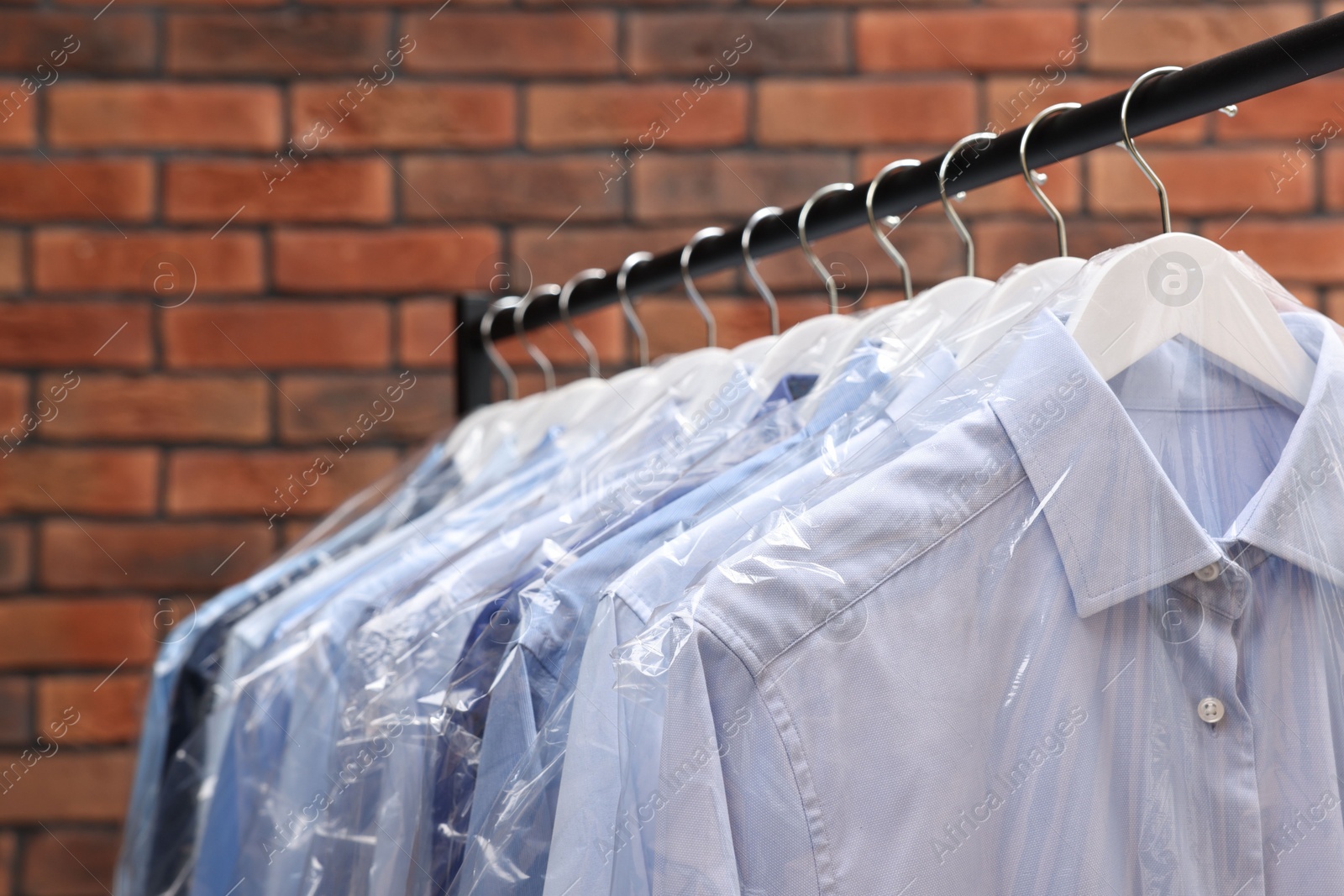 Photo of Dry-cleaning service. Many different clothes hanging on rack against brick wall, closeup