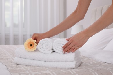 Chambermaid putting flower with fresh towels in hotel room, closeup