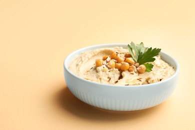 Photo of Bowl of tasty hummus with chickpeas and parsley on beige background. Space for text