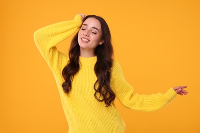 Beautiful young woman in stylish warm sweater on orange background