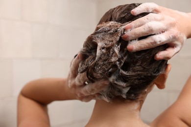 Woman washing hair while taking shower at home, back view