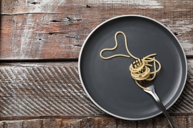 Photo of Heart made of tasty spaghetti and fork on wooden table, top view. Space for text